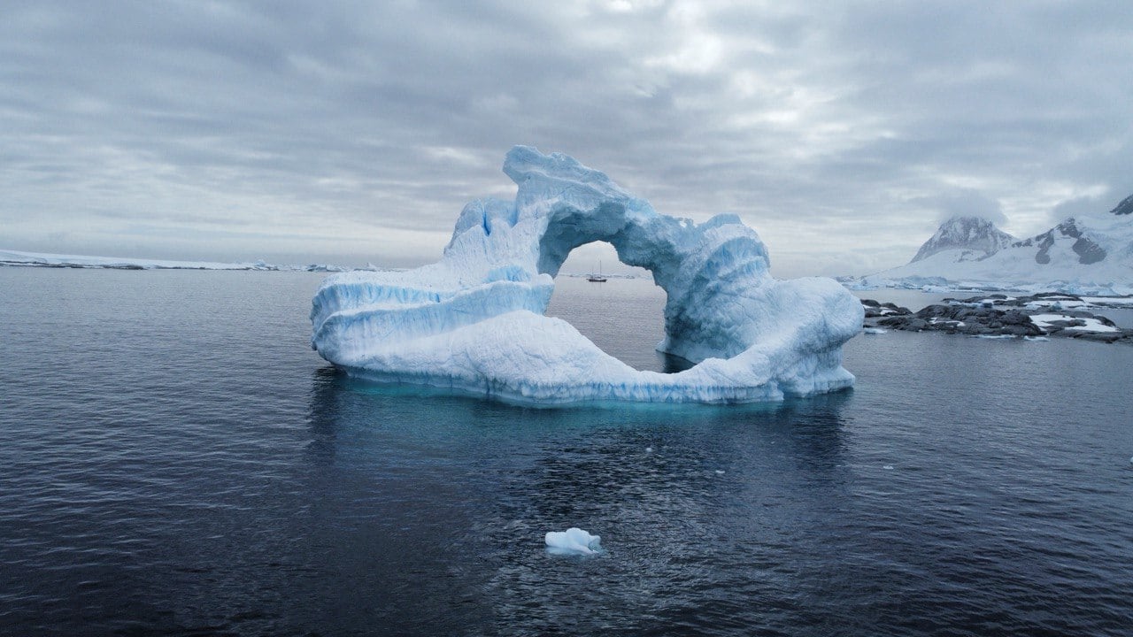 Bogenförmiger blauer Eisberg im antarktischen Wasser